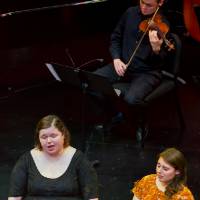 Two women singing and a man playing the violin.